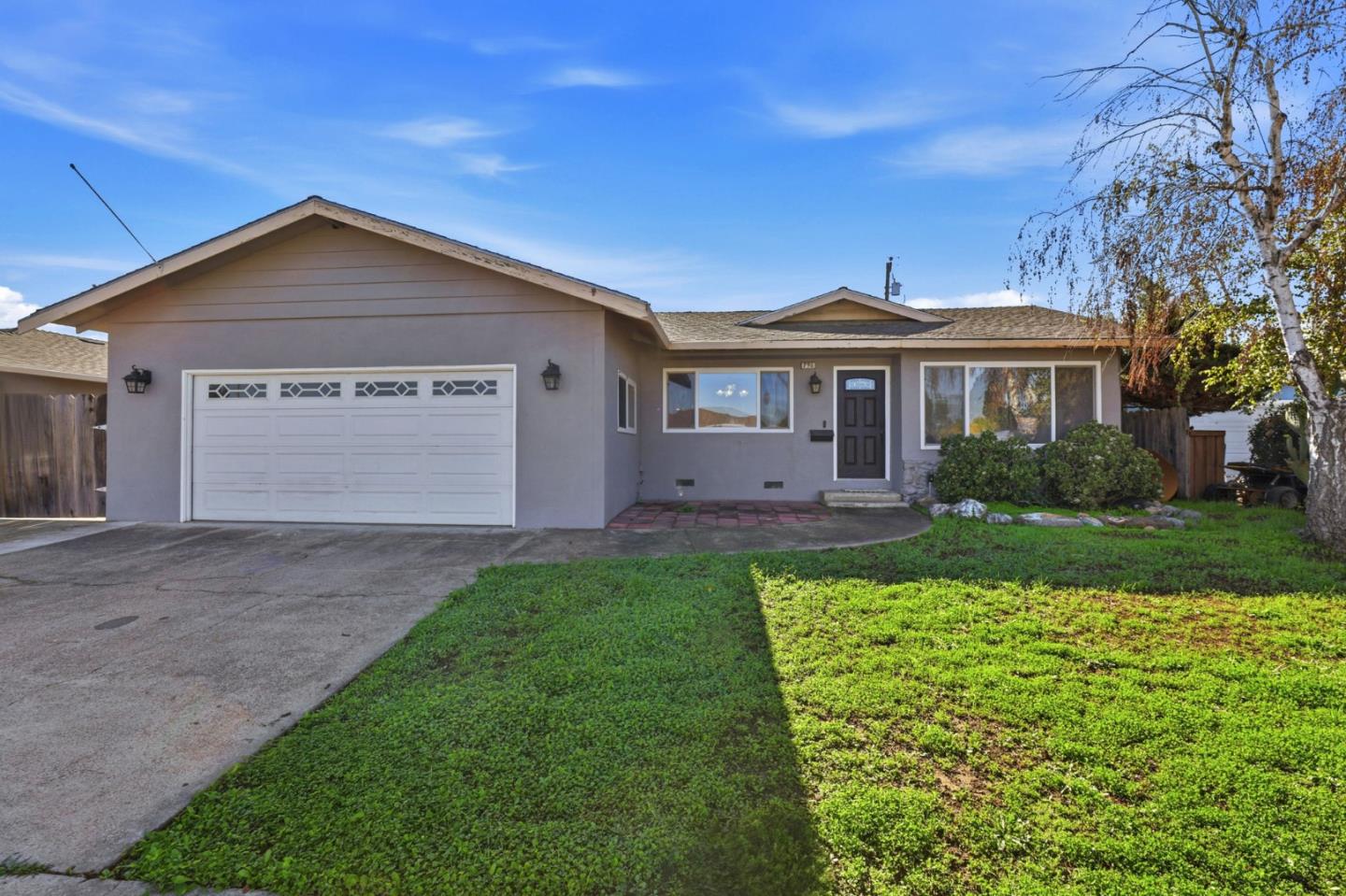 Single-story gray home with a two-car garage, driveway, and green front lawn.