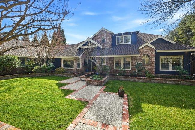 Brick-front house with dark blue siding, a landscaped lawn, and a brick-edged walkway.