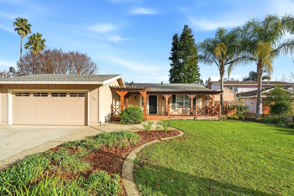 Single-story home with a two-car garage, covered wooden porch, and landscaped front lawn.