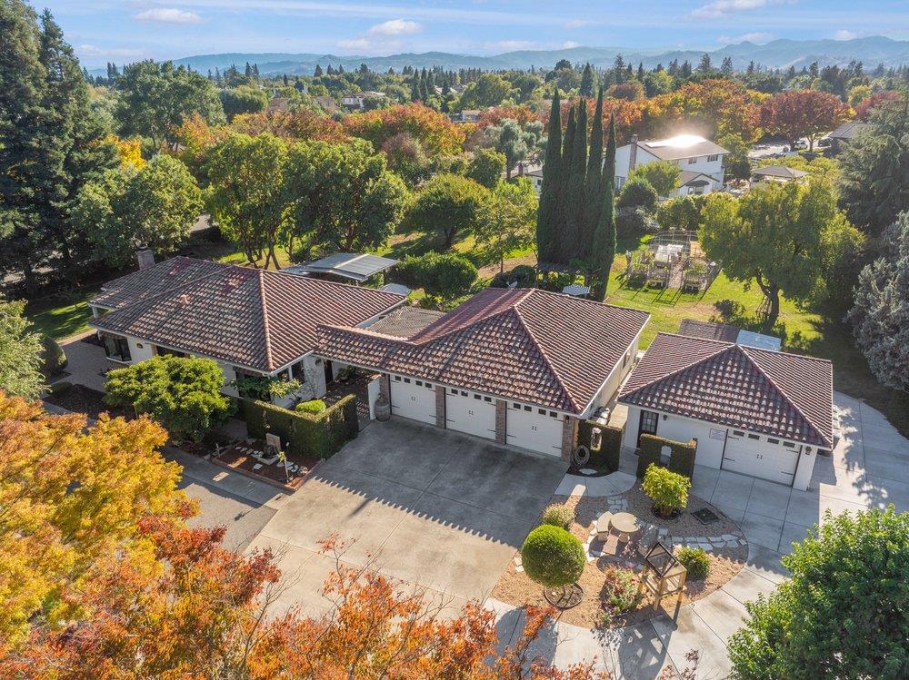 Aerial view of a tile-roofed home surrounded by autumn foliage, with mountains in the distance.