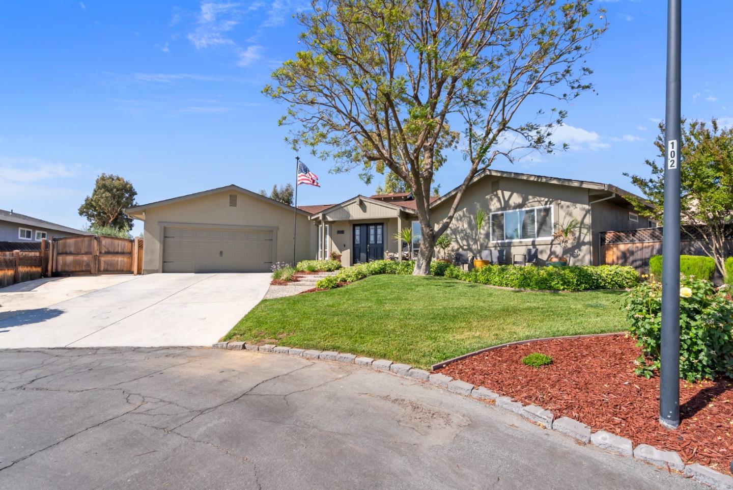 Single-story home with a two-car garage, landscaped front lawn, and large shade tree.