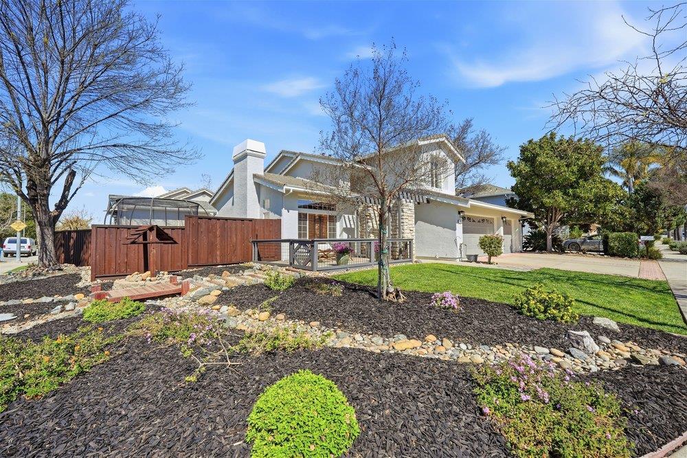 Two-story stucco home with stone accents, a garage, wooden fencing, and a landscaped front yard.
