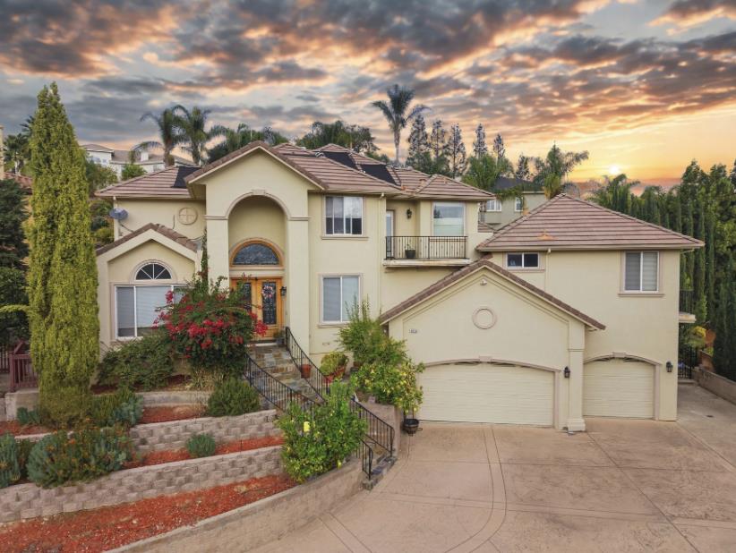 Large stucco home with tiled roofs, landscaped entry, and a broad multi-car driveway at sunset.