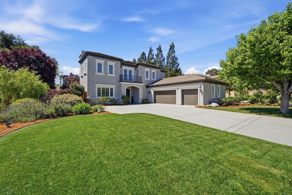 Two-story gray home with an attached two-car garage, balcony, landscaped yard, and broad front lawn.