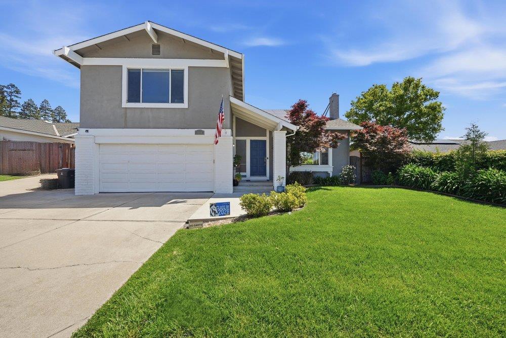 Two-story gray house with a white double garage, blue front door, and broad green lawn.
