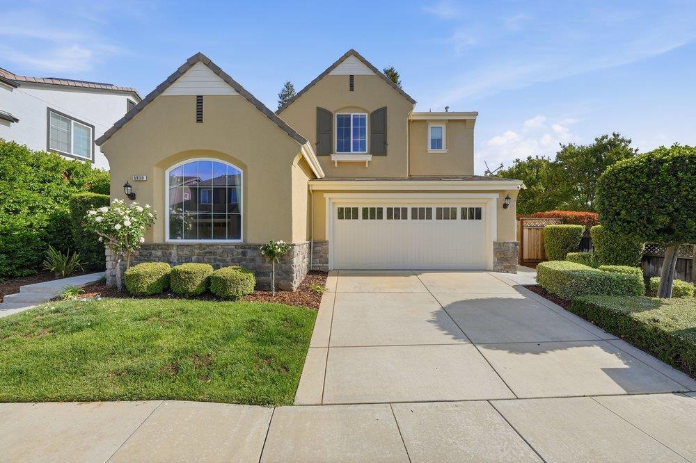 Tan two-story home with stone accents, an arched front window, and an attached two-car garage.