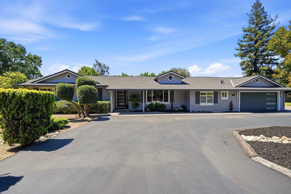 Single-story gray home with a broad driveway, attached garage, and landscaped shrubs.