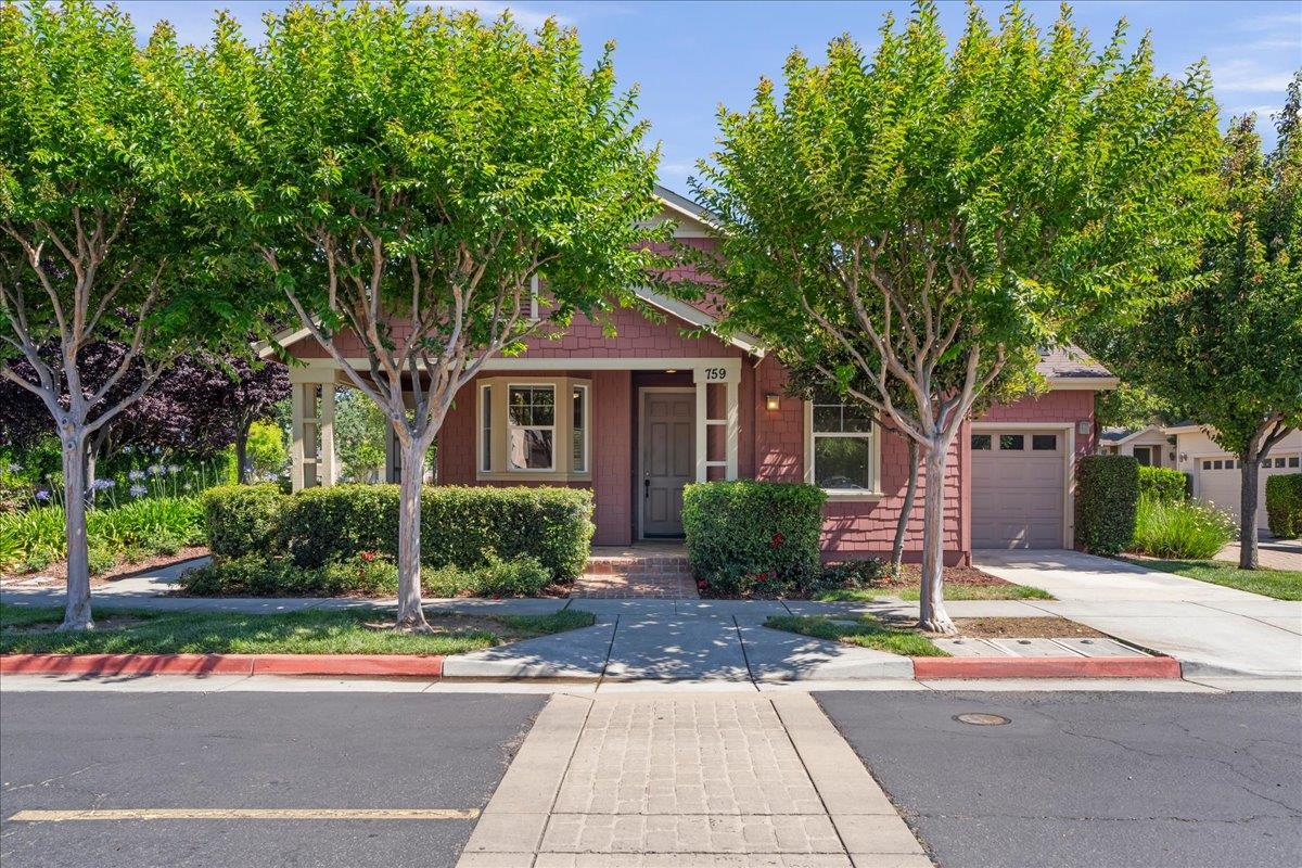 Pink two-story house with a covered porch, attached garage, mature trees, and landscaped front yard.