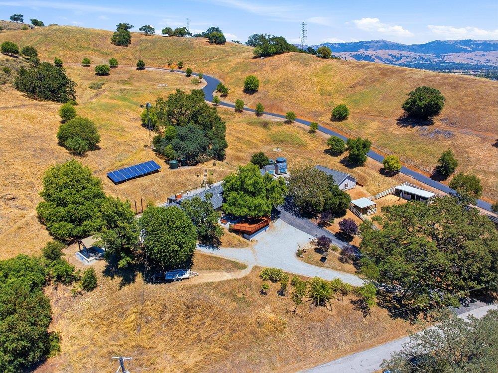 Aerial view of a rural property among dry hills, with a winding road and rooftop solar panels.