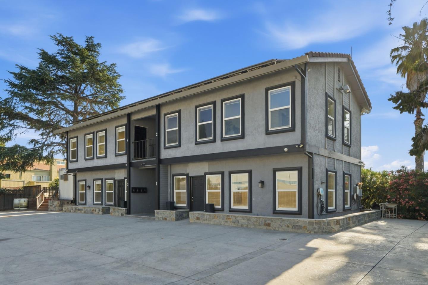 Two-story gray multi-unit building with dark-trimmed windows and a wide concrete driveway.