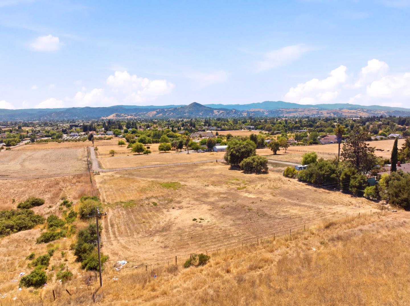 Aerial view of dry open acreage with distant mountain ridges and scattered homes.