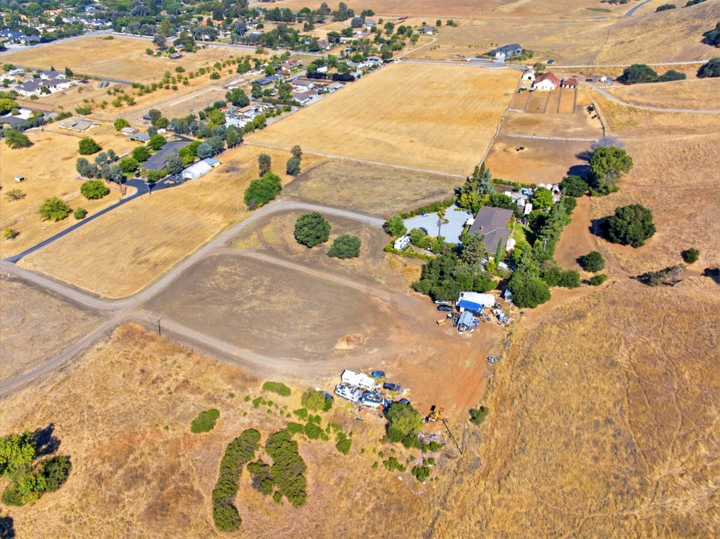 Aerial view of dry open land with dirt access roads, scattered trees, and nearby homes.
