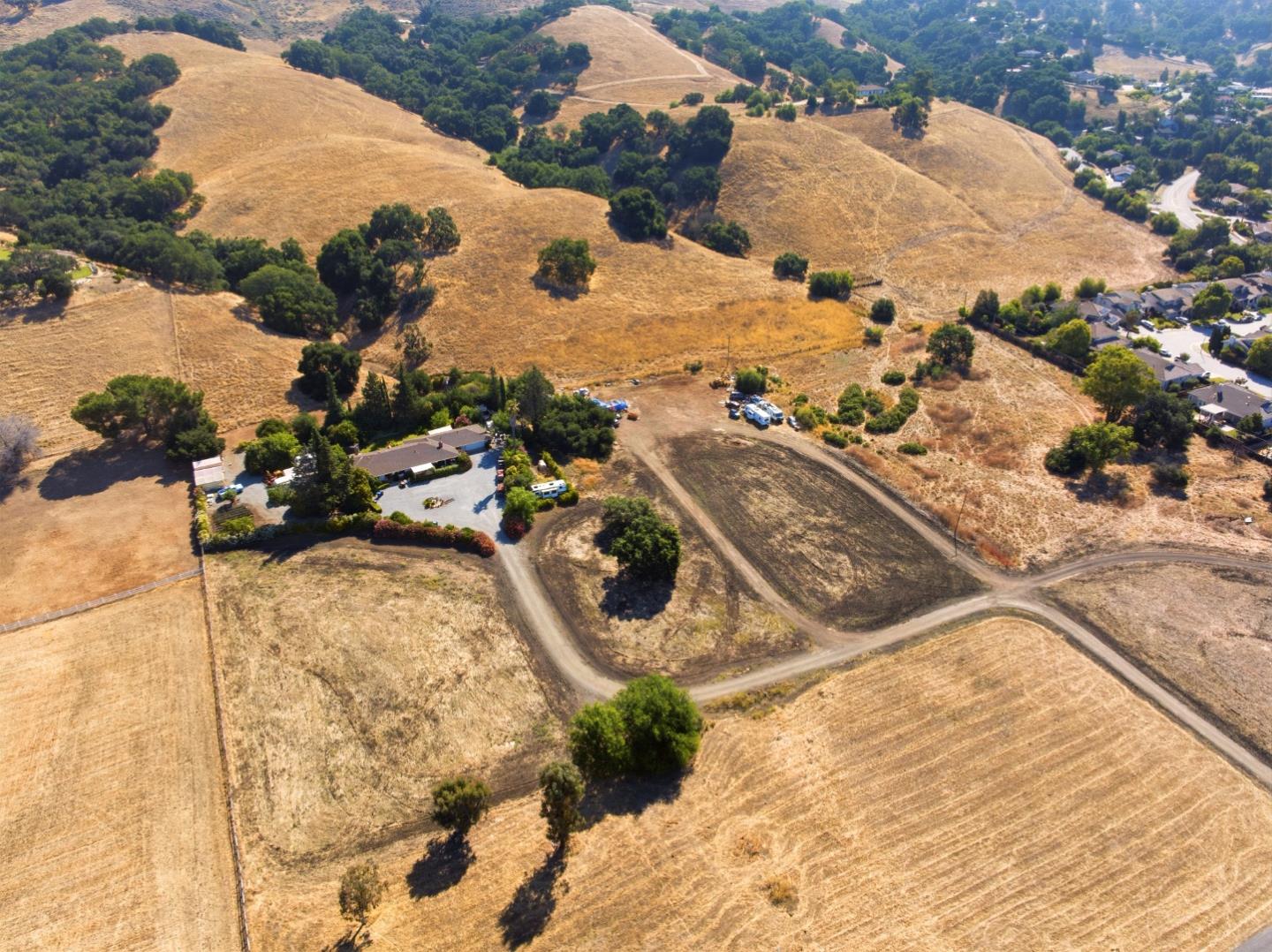 Aerial view of dry rolling land with scattered trees, dirt roads, and nearby homes.