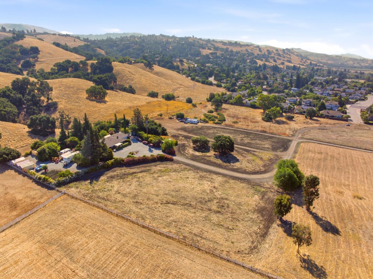 Aerial view of a fenced golden-grass parcel with dirt tracks, nearby homes, and rolling hills.