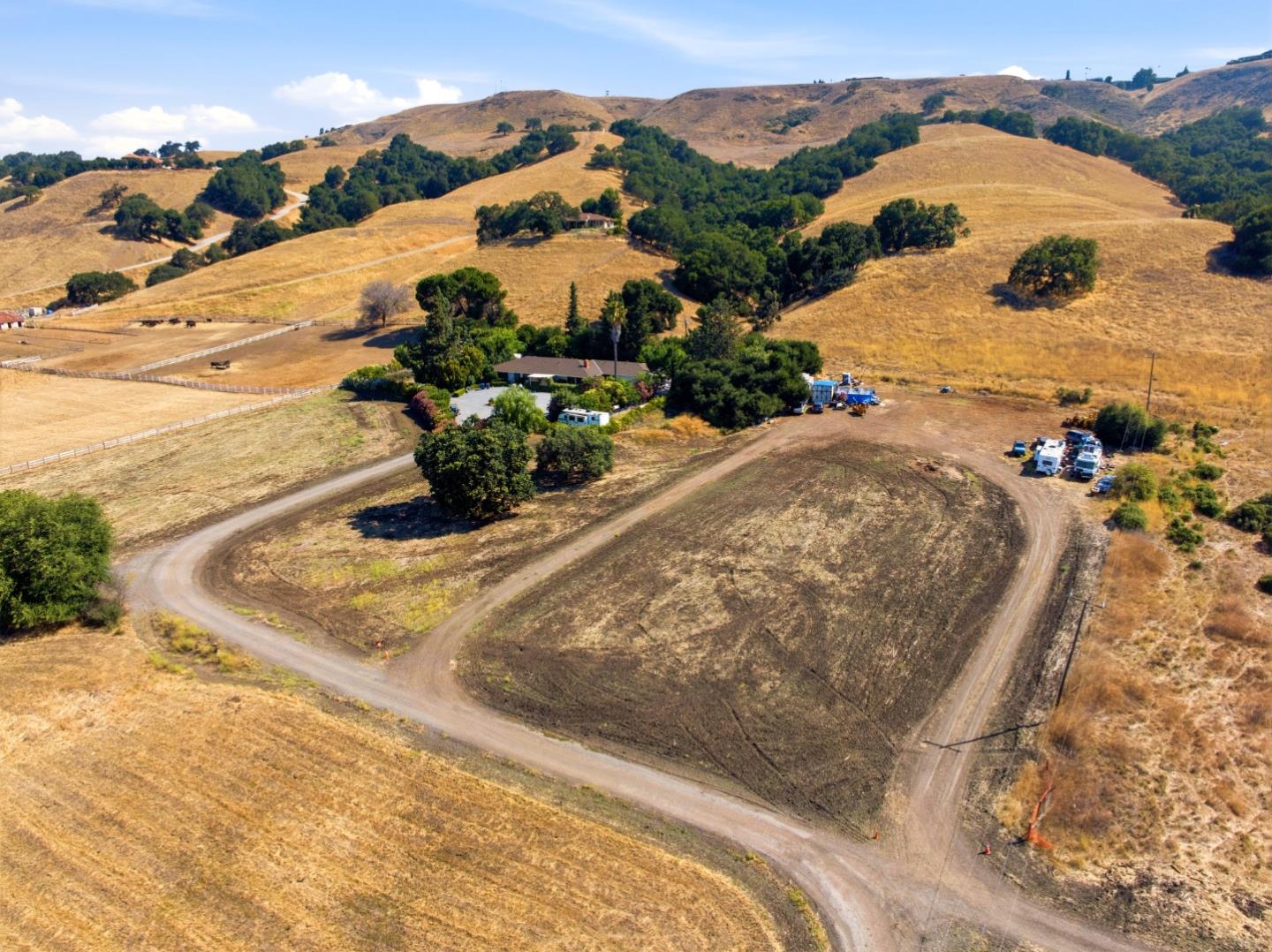 Aerial view of a rural property with a home, outbuildings, and dirt roads amid dry rolling hills.