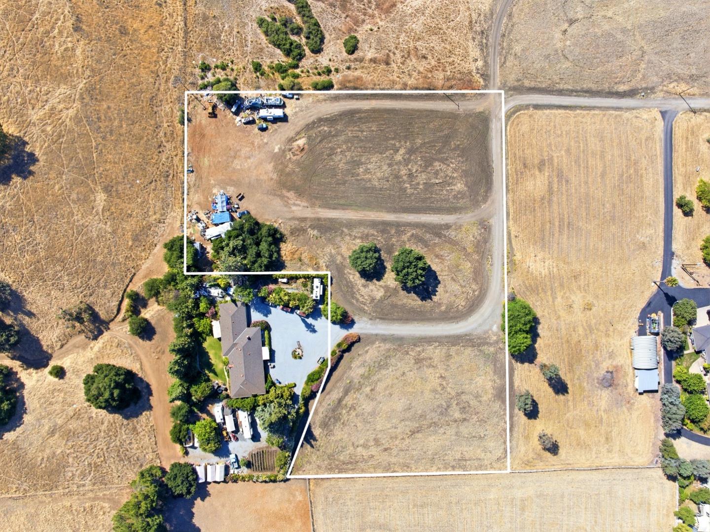 Aerial view of a vacant parcel outlined in white beside a home and dry fields.