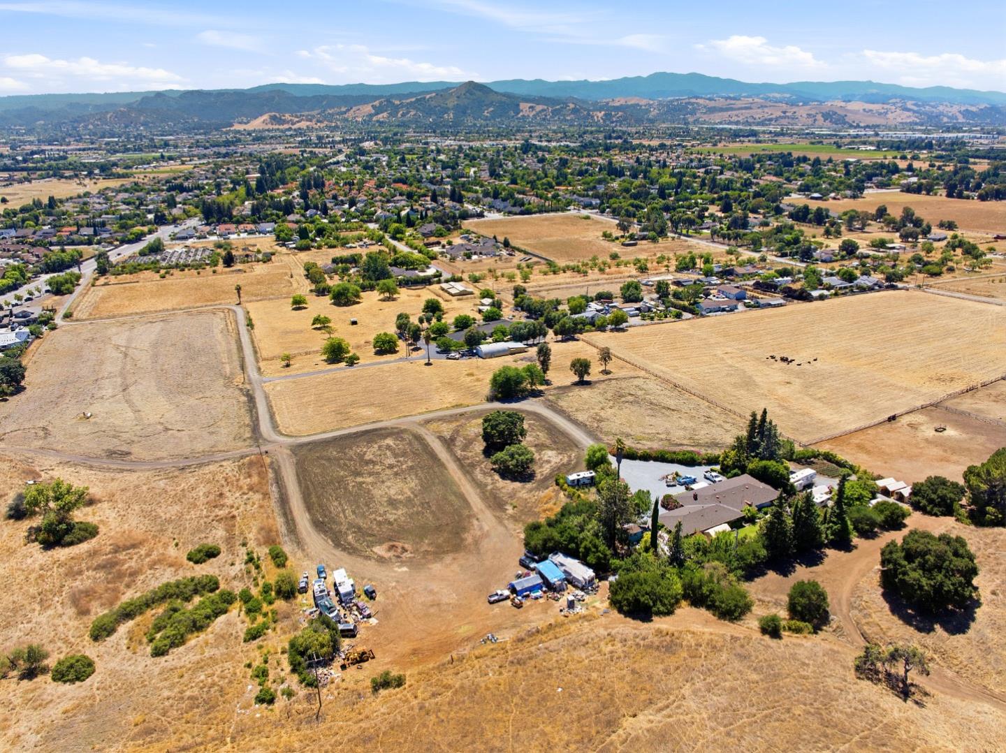 Aerial view of open dry land with dirt tracks, scattered trees, and mountains in the distance.