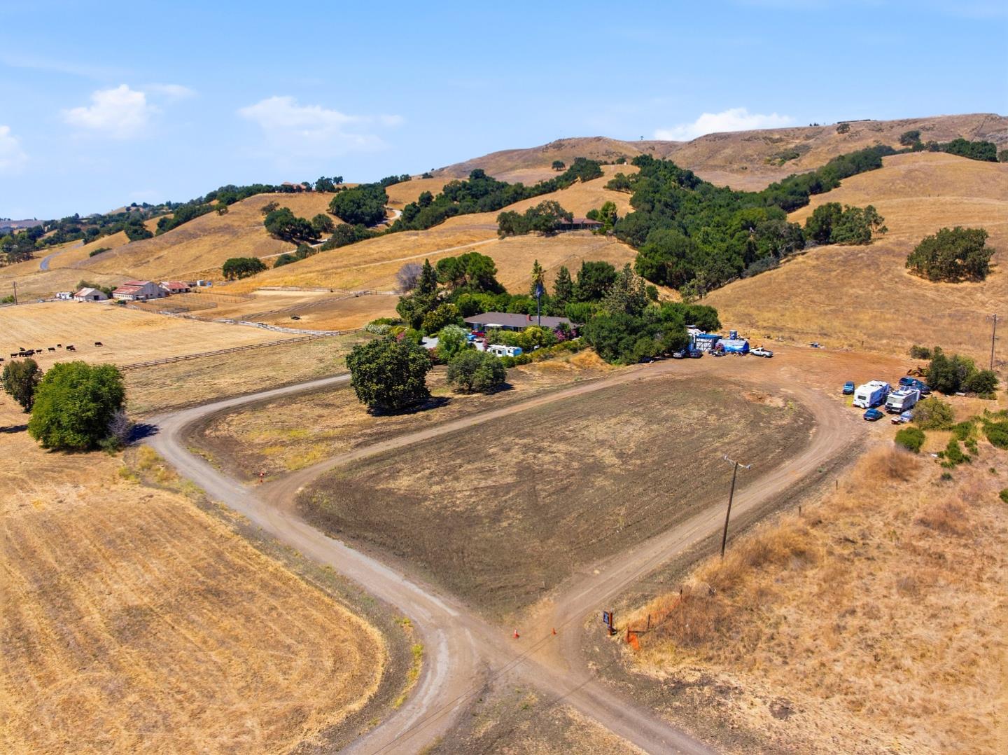 Aerial view of a rural property with a looping dirt drive, scattered buildings, and dry golden hills.