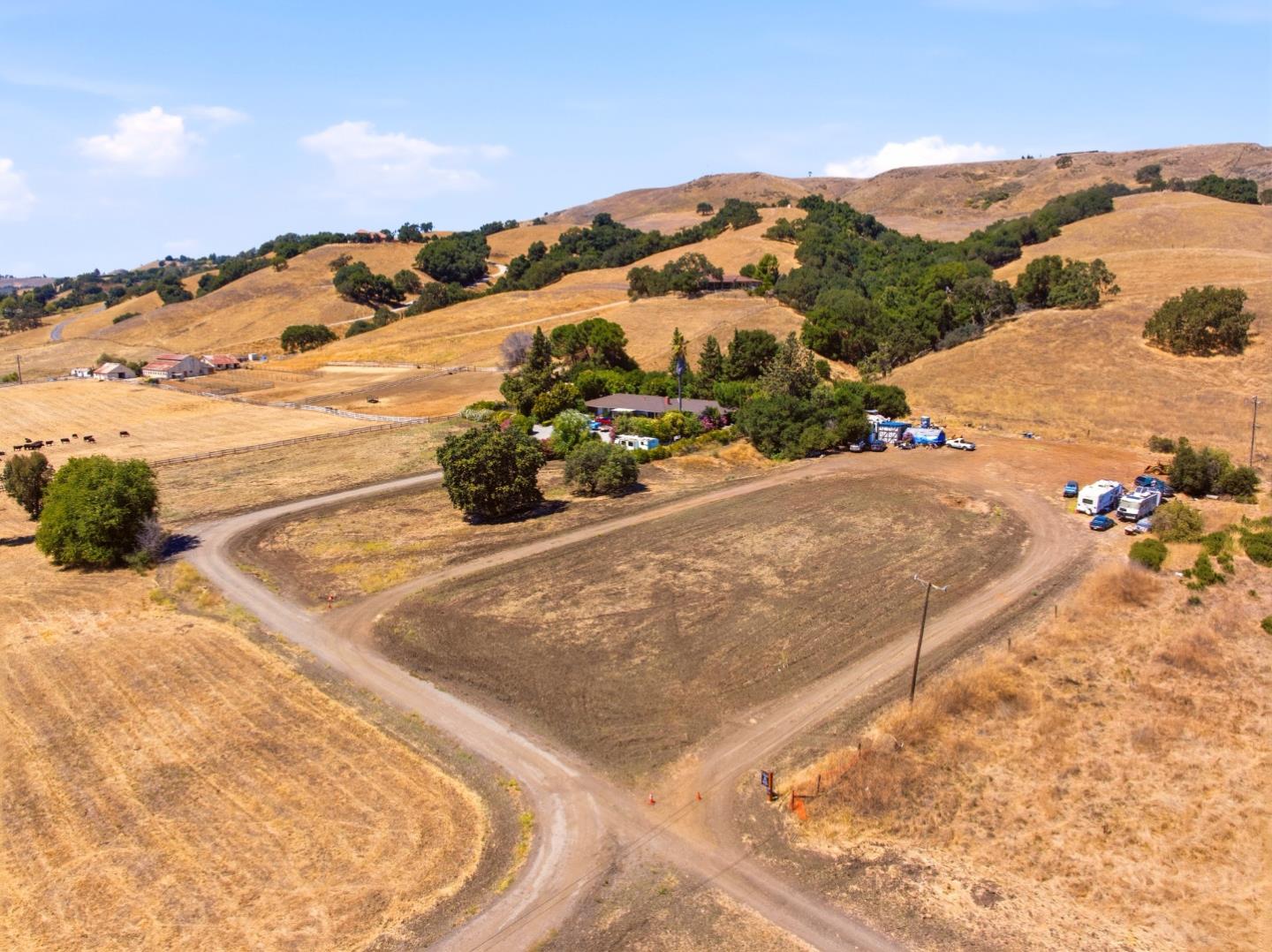 Aerial view of dry rolling acreage with dirt roads, scattered trees, and buildings.