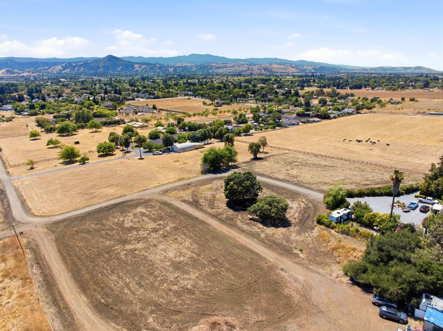 Aerial view of a dry vacant parcel with dirt tracks, fields, and distant hills.