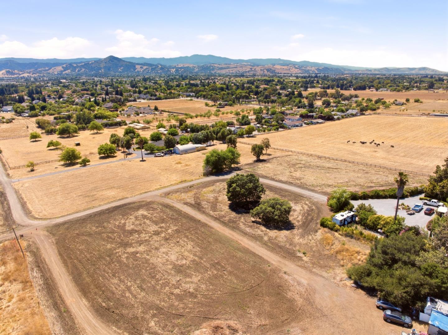 Aerial view of dry open land and scattered rural homes, with mountains in the distance.