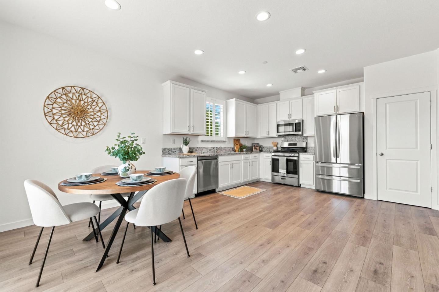 Bright kitchen and dining area with white cabinetry, stainless steel appliances, and wood flooring.