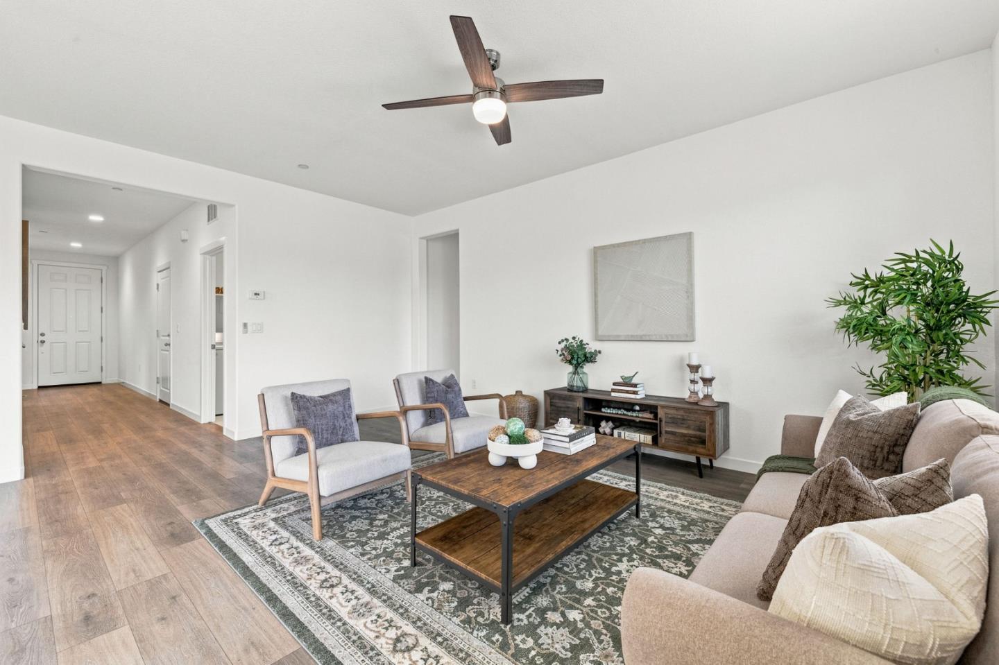 Staged living room with a beige sofa, wood coffee table, patterned rug, and ceiling fan.