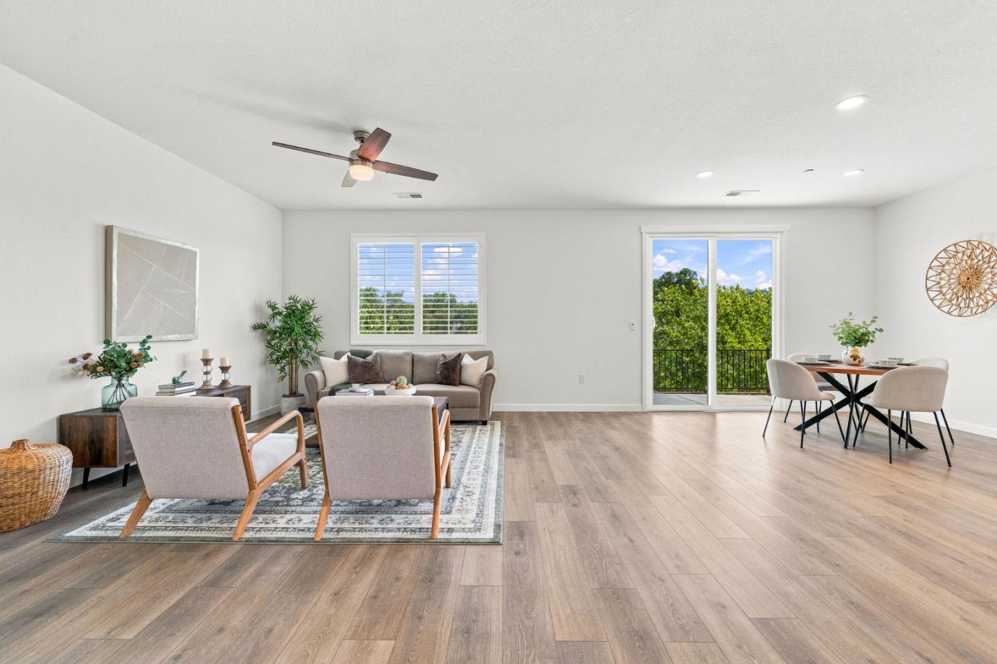 Staged living and dining room with wood floors and sliding doors to a leafy balcony.