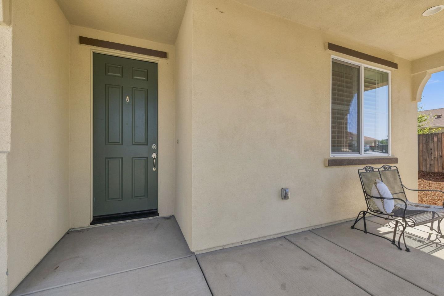 Home entry porch with a dark green front door, large window, and metal patio seating.