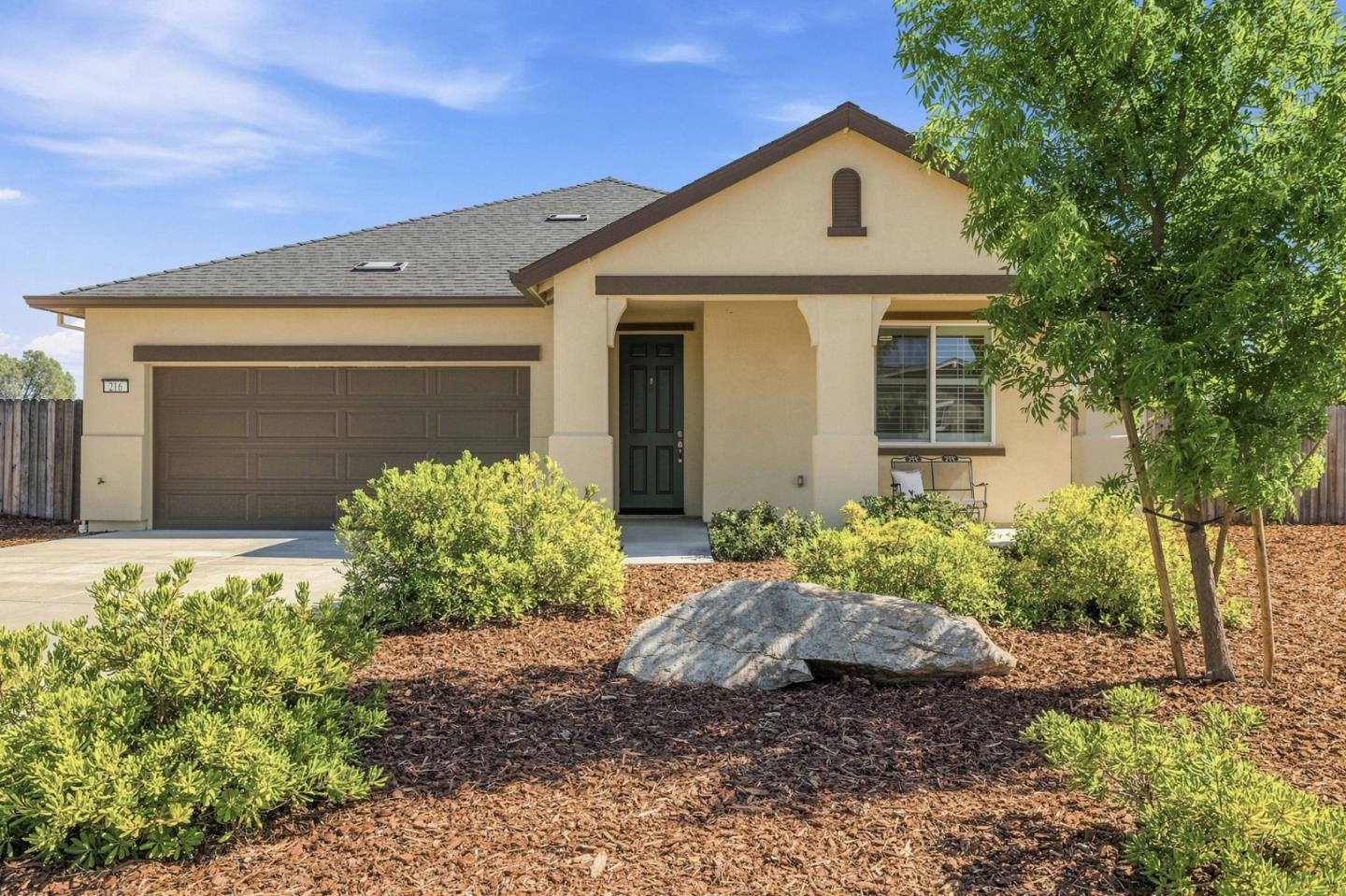 Beige stucco home with a dark two-car garage, covered entry, and landscaped front yard.