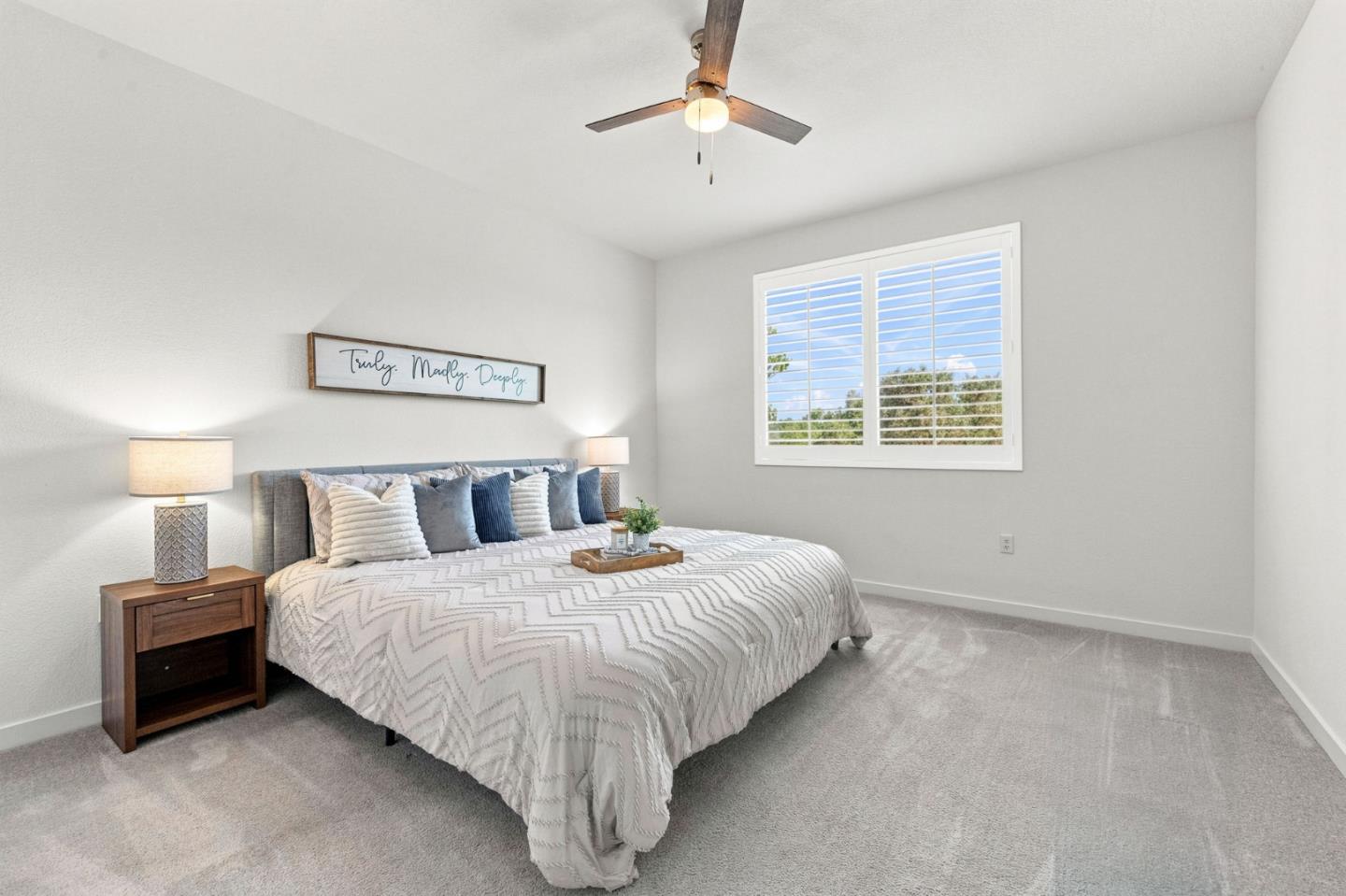 Bedroom with a white patterned bedspread, blue pillows, and a shuttered window.