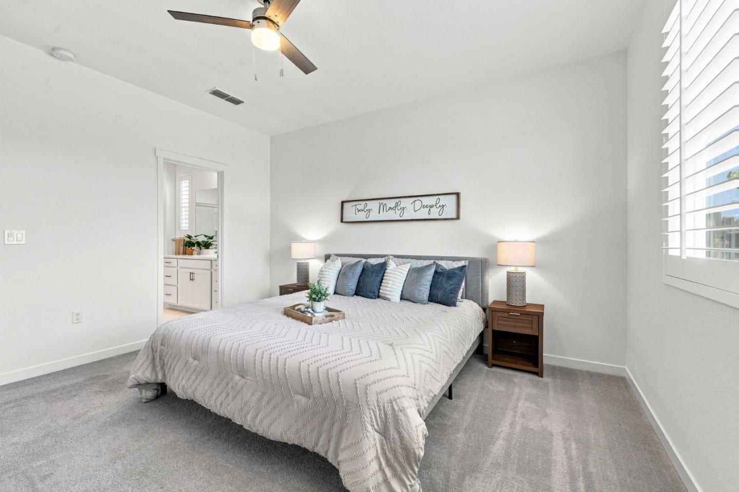 Staged bedroom with a large bed, layered blue and white pillows, and white plantation shutters.