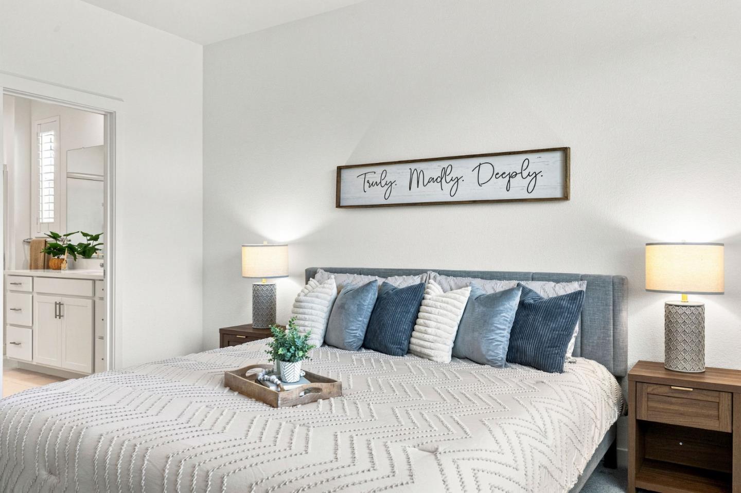 Furnished bedroom with a large white-quilted bed, layered blue pillows, and a framed sign above the headboard.