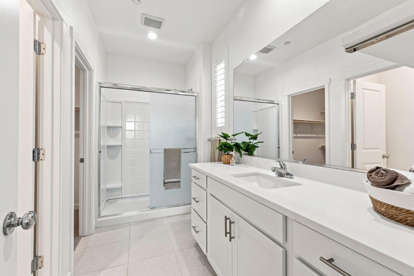 Bright white bathroom with a long vanity, large mirror, and glass-enclosed shower.