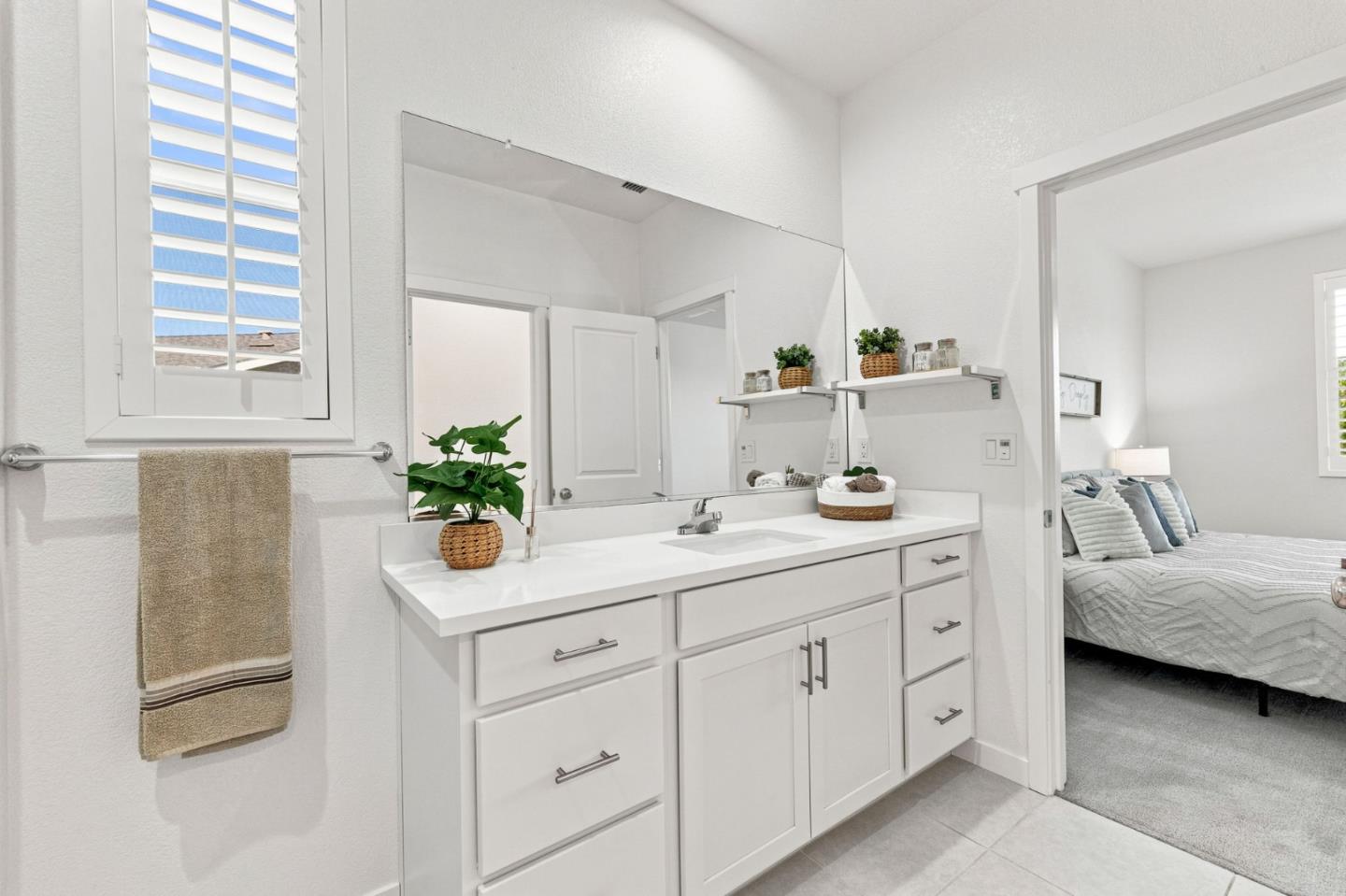 Bathroom with a white vanity, large mirror, and doorway to a bedroom.