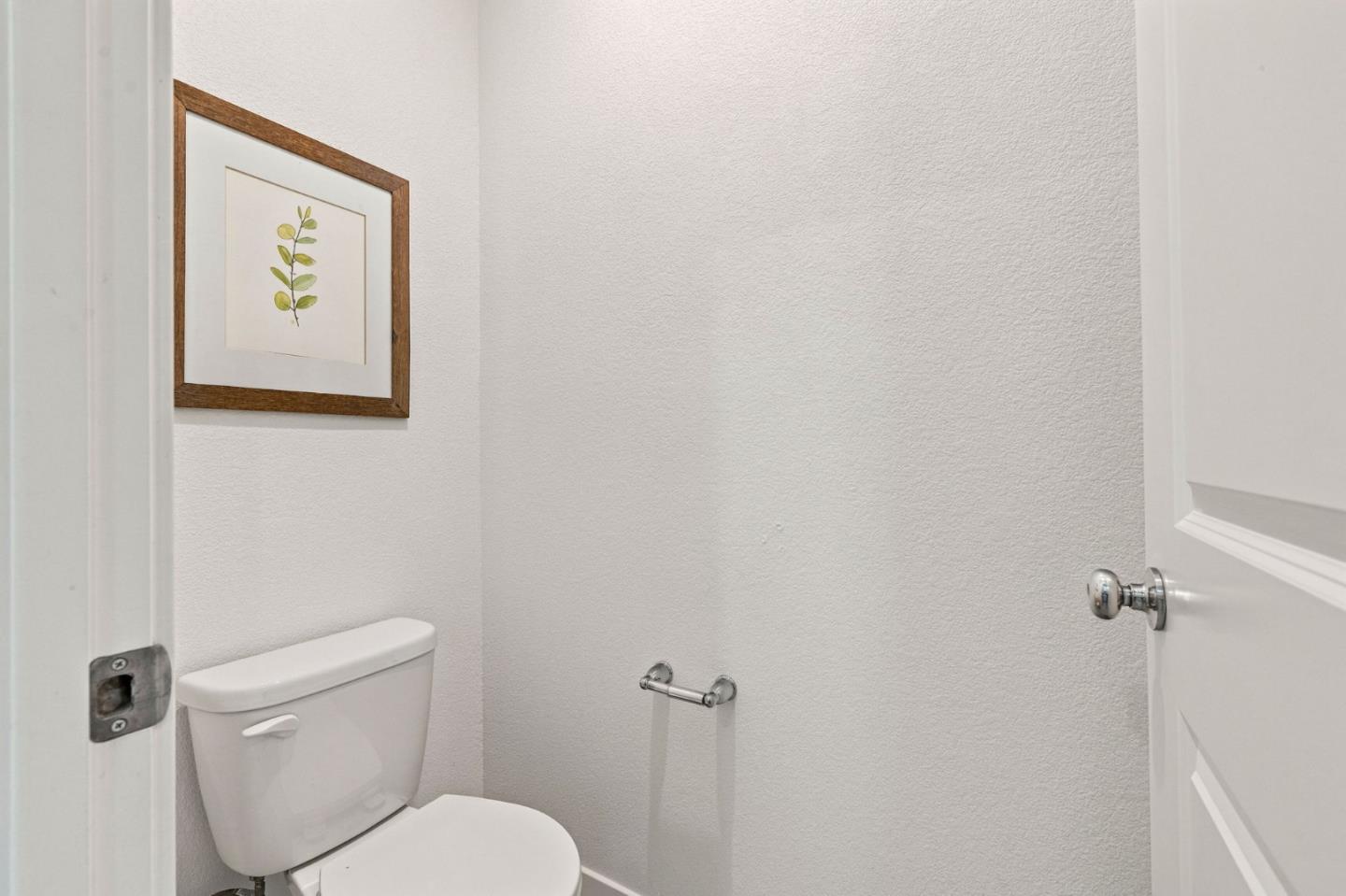 Bathroom with a white toilet and framed botanical print.