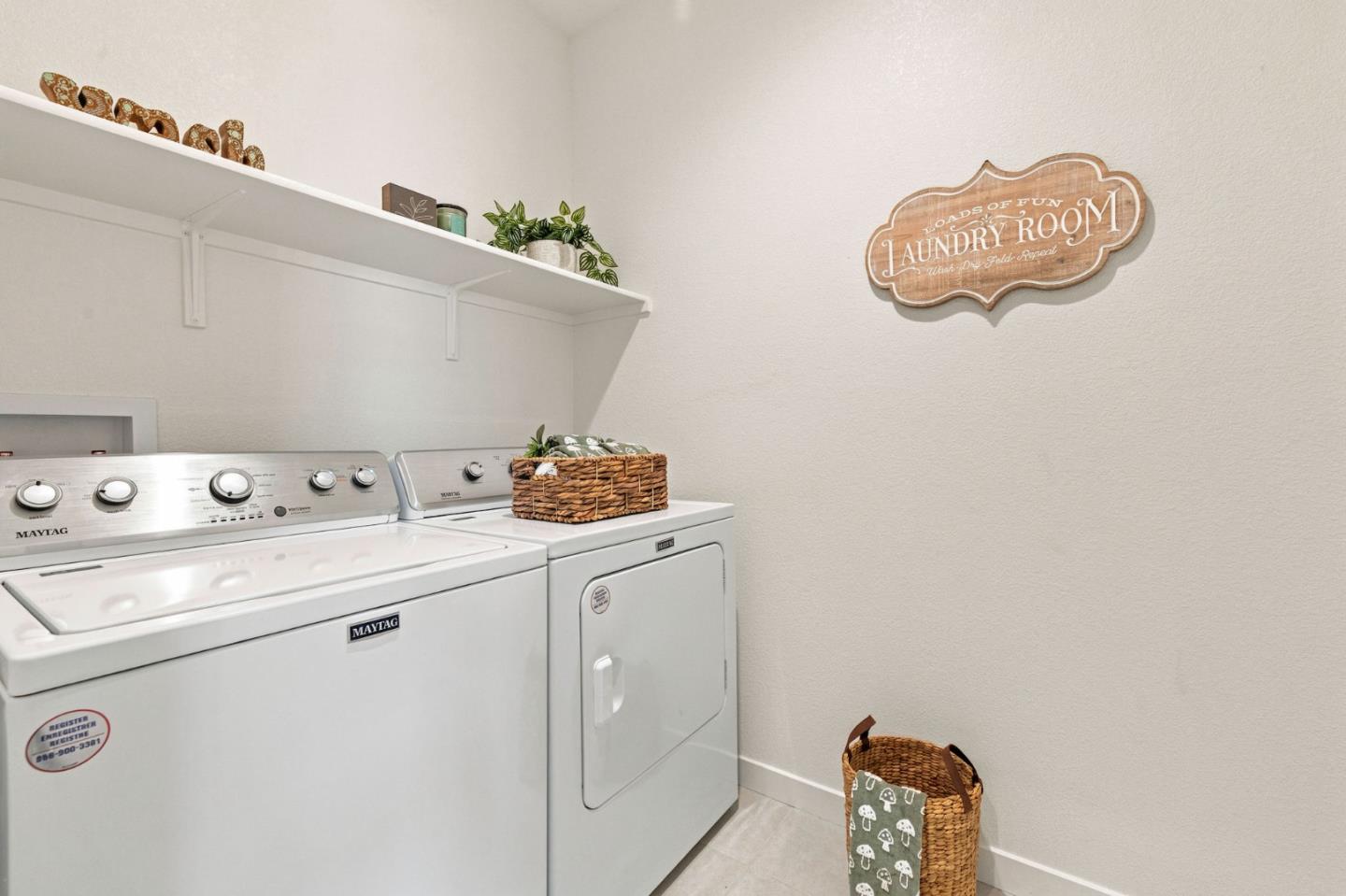 Laundry room with a white washer and dryer, wall shelf, plants, and decorative sign.
