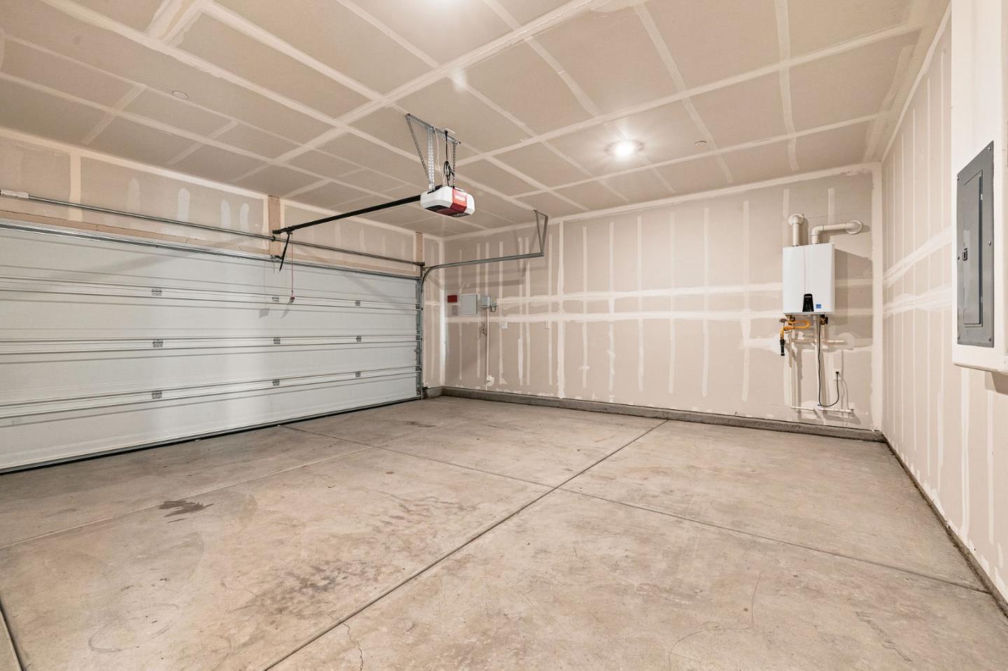 Empty garage with unfinished drywall, concrete floor, overhead door, and wall-mounted water heater.