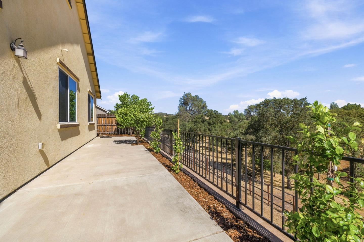 Concrete patio beside a tan stucco house, bordered by a black railing and trees.