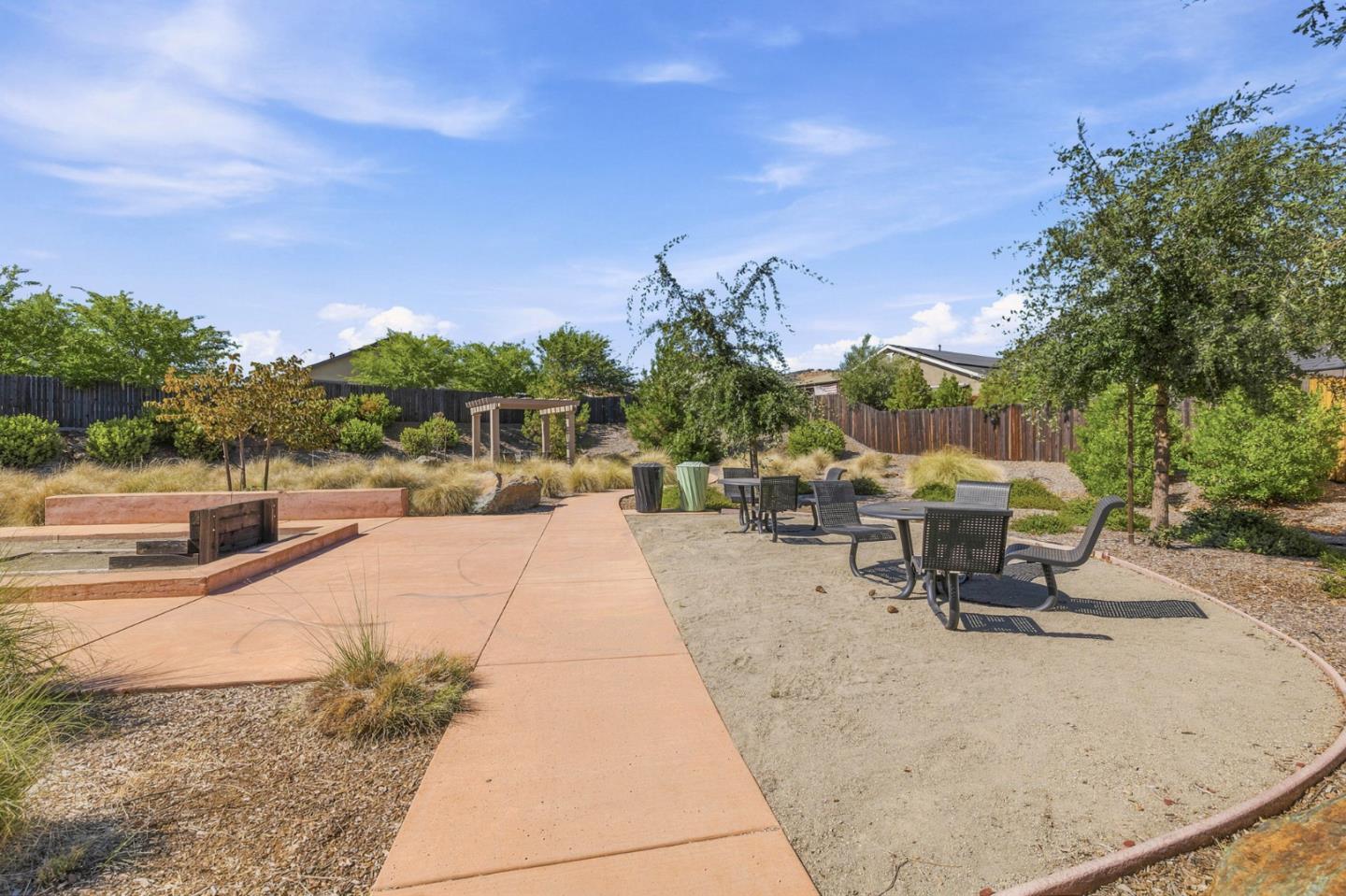 Landscaped courtyard with a built-in fire pit and picnic tables beside a curved walkway.