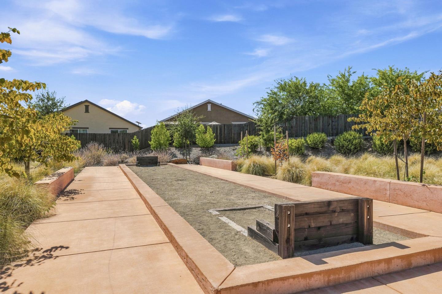 Landscaped yard with concrete paths, a wooden raised planter, ornamental grasses, and a tall fence.