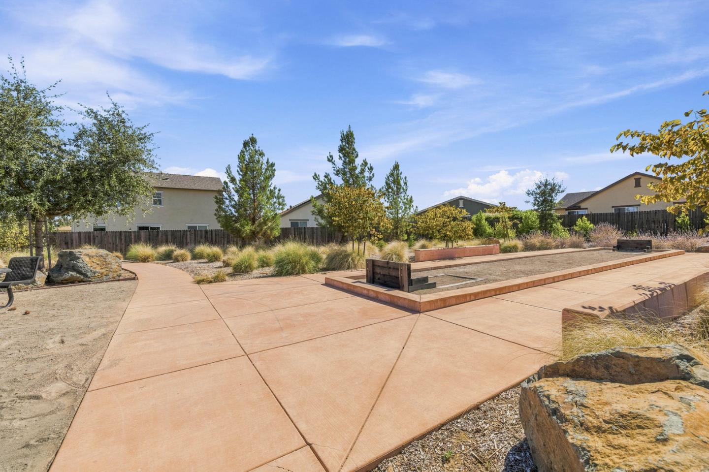 Landscaped patio with a long bocce ball court, concrete paving, and ornamental grasses.