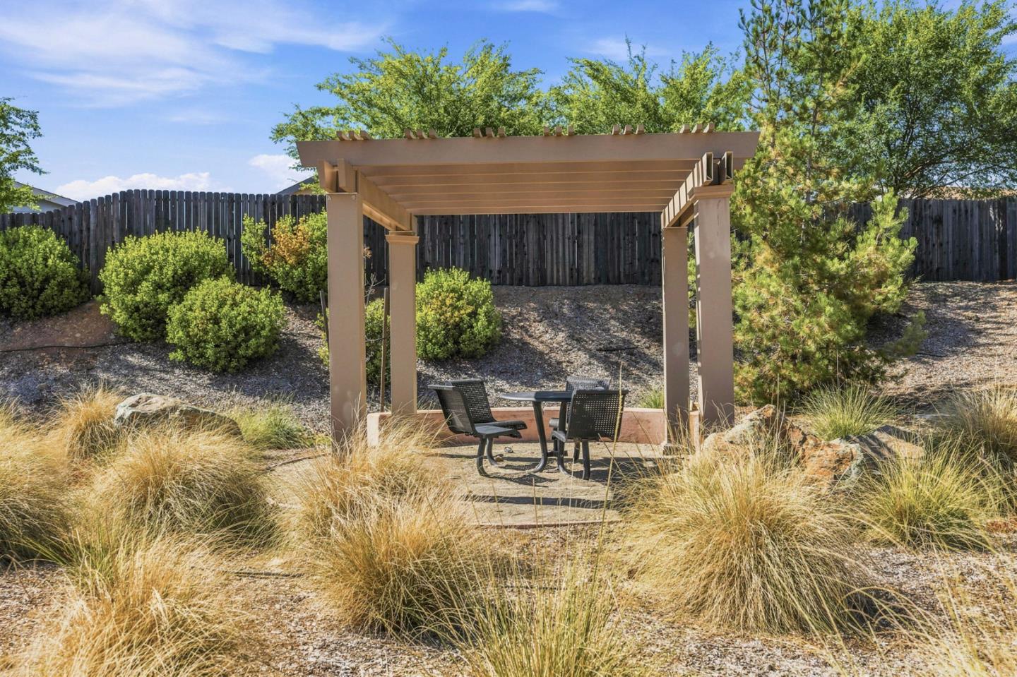 Backyard patio with a wooden pergola, outdoor table and chairs, gravel landscaping, and mature trees.