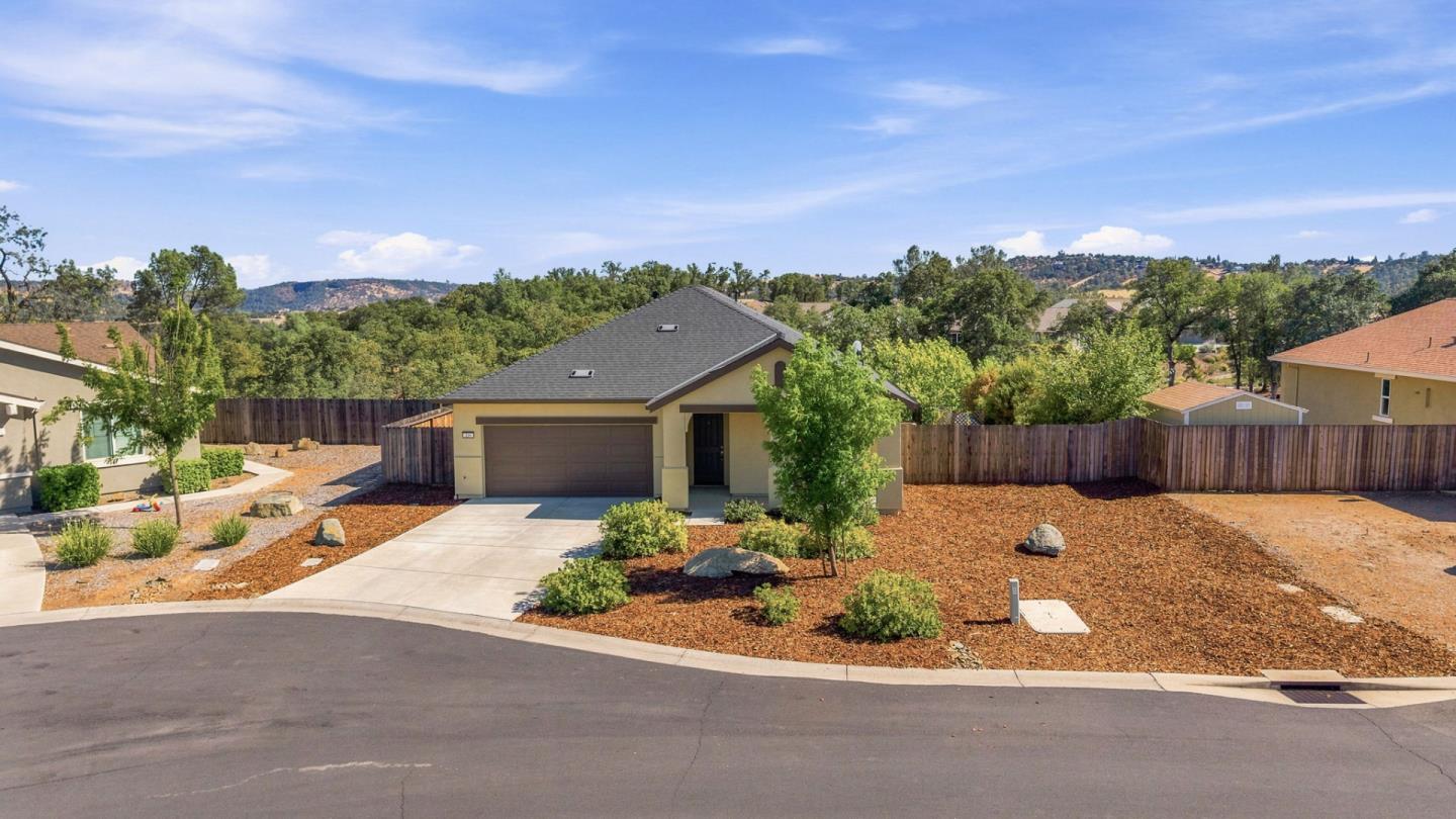 Single-story beige home with a two-car garage, landscaped yard, and hills in the background.