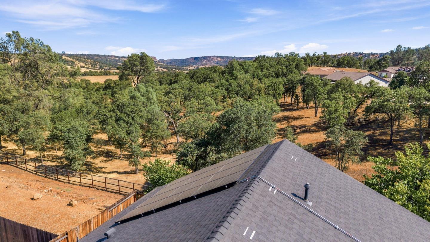 Home roof with solar panels overlooking oak trees, neighboring houses, and distant hills.