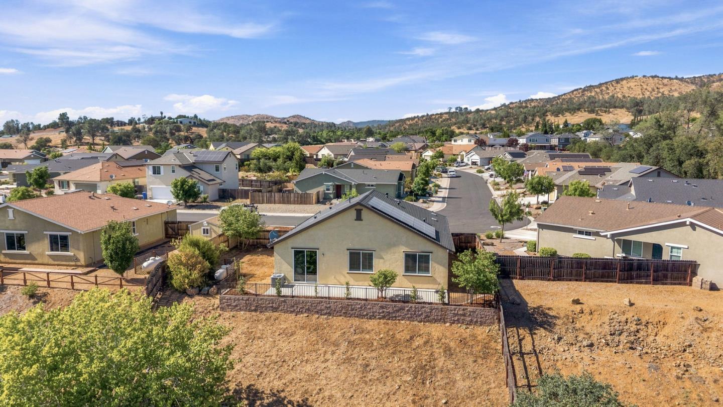Aerial view of a single-story home with a fenced, dry backyard in a hillside neighborhood.