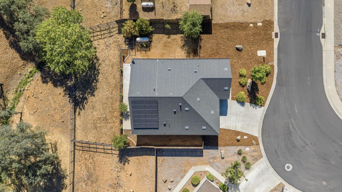 Aerial view of a home with rooftop solar panels and a fenced yard beside a curved street.