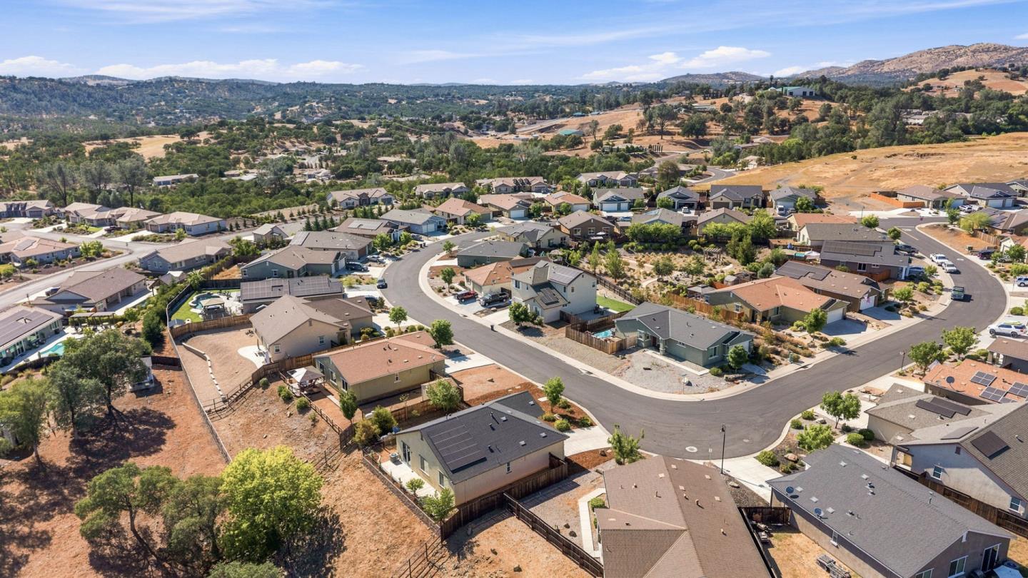 Aerial view of homes along a curving street, with dry hills in the distance.