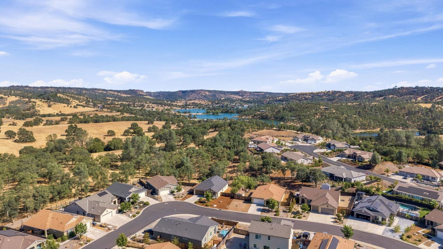 Aerial view of homes along curving streets, with a distant lake and wooded hills.