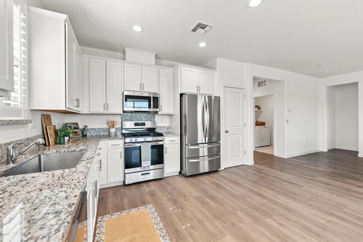 Bright kitchen with white cabinets, speckled stone counters, stainless appliances, and plantation shutters.